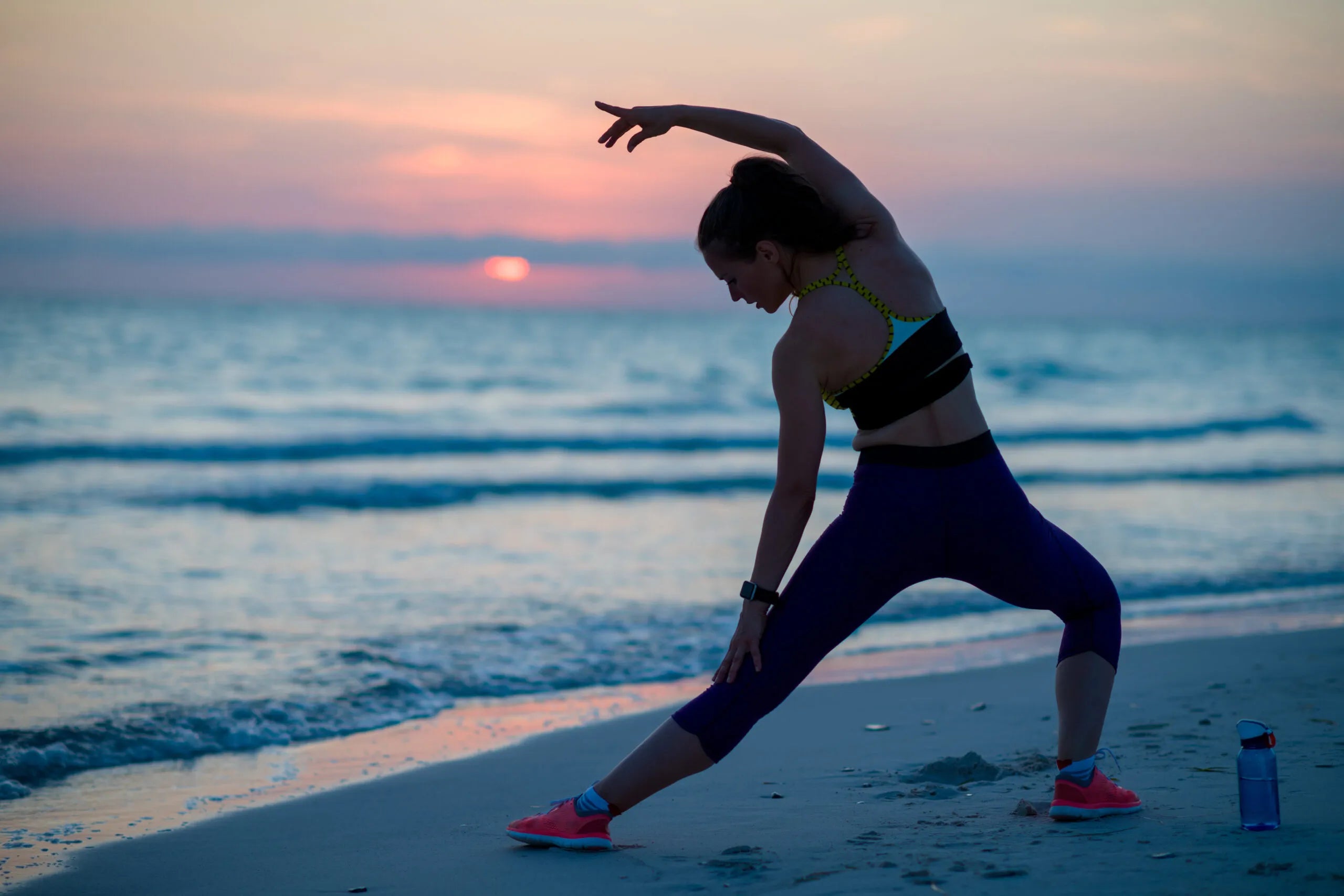 Woman stretching on the beach at sunset to support flexibility, mobility and active recovery