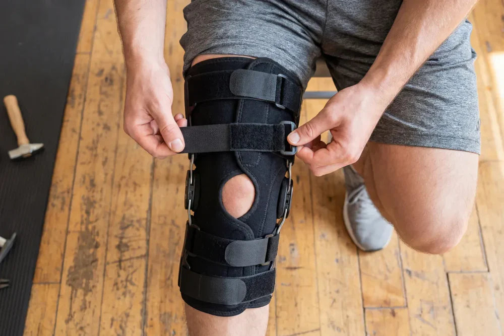 Person adjusting a knee brace for support during recovery from knee injury and rehabilitation