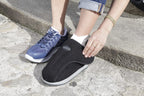 Woman adjusting black Darco mesh recovery shoe on stone steps, wearing blue athletic sneaker on other foot